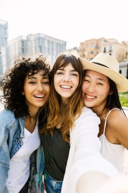 Üç farklı kadından oluşan genç bir grup açık havada telefonla selfie portresi çekiyor. Neşeli milenyum bayan arkadaşları hafta sonları şehir sokağında tatilin tadını çıkarıyorlar. Arkadaşlık kavramı