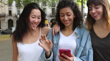 Bir grup mutlu genç kadın şehirde yürürken cep telefonu kullanarak eğleniyor..