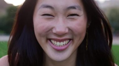 Açık havada gülümseyen Asyalı genç kadın portresi. Mutlu Milenyum Çinli kadın şehir parkında kameraya bakıyor..