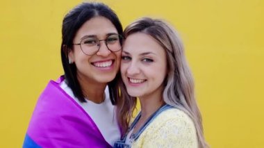 Sarı arka planda birbirlerine gülümseyen sevimli lezbiyen çiftin portresi. LGBTQ ve aşk konsepti