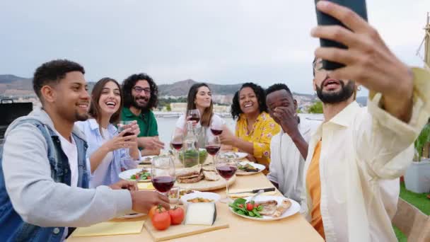 ハウステラスでバーベキューディナーパーティーを楽しむ多人種の友人の幸せな若いグループ 誕生日のお祝いの間に携帯電話で自撮り写真を撮る千年の陽気な男性と女性 — ストック動画