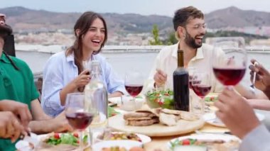 Gülümseyen bir grup arkadaş çatıdaki partide yemek yiyorlar. Mutlu bin yıllık çok ırklı insanlar gülerek ve eğlenirken yaz kutlamalarında masada oturup yemek yerken..