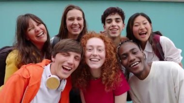 Çeşitli öğrenci arkadaşlar mavi arka planda yan yana duruyorlar. Üniversiteli gençlerin, kameraya gülümserken eğlendikleri portresi. Gençlik toplumu ve arkadaşlık kavramı