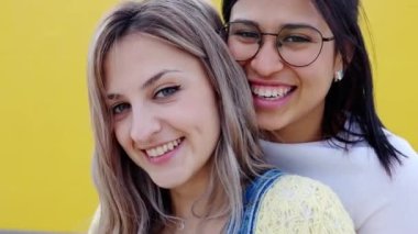 Gülümseyen genç lezbiyen çiftin portresi sarı arka planda birbirlerine sarılıyorlar. LGBTQ insanları kavramı.