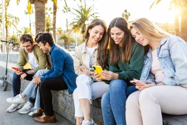 Dışarıda cep telefonu kullanan bir grup genç arkadaş. Millennials akıllı telefon uygulamasında sosyal medya içeriğini izlerken eğleniyor. Teknoloji ve gençlik toplumu kavramı.