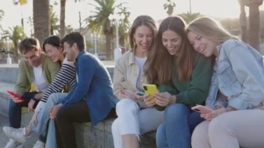 Dışarıda cep telefonu kullanan bir grup genç arkadaş. Millennials akıllı telefon uygulamasında sosyal medya içeriğini izlerken eğleniyor. Teknoloji ve gençlik toplumu kavramı.