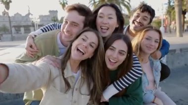 Şehir caddesinde cep telefonuyla selfie çeken mutlu genç bir grup insan. Genç kızlar ve erkekler gün batımında tatilin tadını çıkarıyorlar. Arkadaşlık, gençlik ve genel z insanları kavramı.
