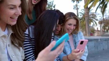 Açık havada akıllı cep telefonu kullanan bir grup genç öğrenci. Genç erkekler ve kızlar cep telefonu ekranındaki sosyal medya içeriğine bakarak eğleniyorlar. Teknoloji yaşam tarzı konsepti