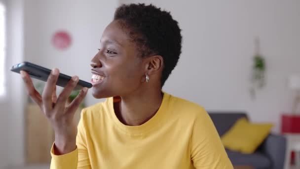 若いアフリカの女性は 自宅からノートパソコンで作業しながら 友人に音声音声メッセージを録音するために携帯電話アプリを使用しています テクノロジーと若者文化の概念 — ストック動画