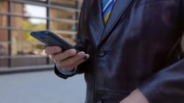 Şehir caddesinde yürürken akıllı telefon kullanan işadamının yakın görüntüsü. Uygulamada sosyal medya içeriğini kaydırırken çevrimiçi mesajlaşma, cep telefonu ekranına kaydırma ve dokunma.