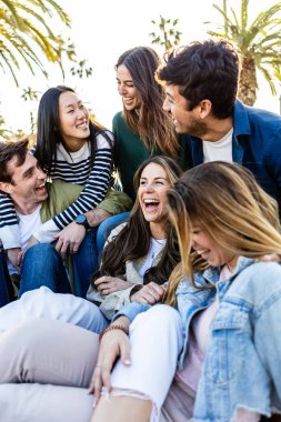 Dışarıda otururken eğlenen bin yıllık mutlu arkadaş grubunun dikey fotoğrafı. Çeşitli üniversite öğrencileri birlikte gülüyor ve gülüyor. Sokakta birlikte rahatlıyorlar. Arkadaşlık ve gençlik yaşam tarzı konsepti.