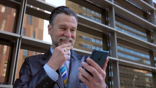 携帯電話で良いニュースを受信成功した高級ビジネスマンは 勝利のジェスチャーで達成を祝う手を握っています 会社のセールスマンは携帯電話で肯定的なオンライン通知を読む — ストック動画