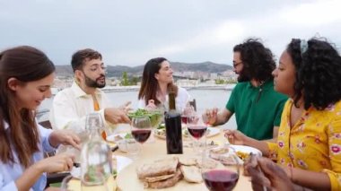 Genç bir grup insan yaz partisinde terasta öğle yemeği yiyor. Mutlu milenyum dostları kutlamak için bir çatı katında toplandı. Arkadaşlık ve kutlama konsepti.