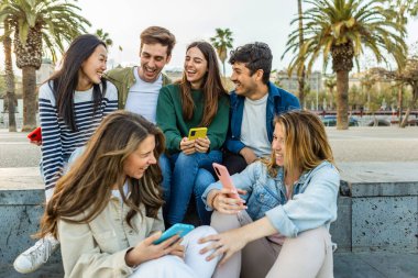 Cep telefonlu mutlu öğrenci grubu dışarıda otururken eğleniyor. Milenyum kuşağından çeşitli arkadaşlar gülerek şehrin sokaklarında sosyal toplantının keyfini çıkarıyorlar. Gençlik yaşam tarzı.