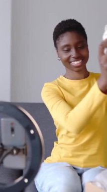 Gülümseyen genç nüfuzlu biri, sosyal medya için eve yeni gelen kıyafetleri gösteren bir video kaydediyor. Milenyum Afrikalı kadın cep telefonu uygulaması kullanarak canlı yayın yapıyor. Eğilim ve gençlik kavramı.