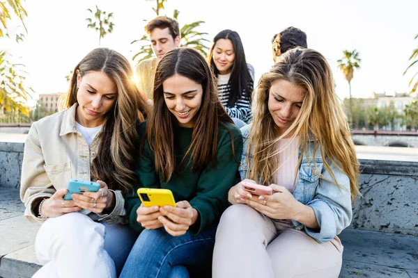 stock image Teenage group of young people looking at smart mobile phone screen outdoors. Addicted millennial student friends using smartphones to watch social media content sitting together in city street.