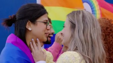 Arka planda LGBT grubuyla öpüşen iki farklı genç kız eşcinsel onur ayı festivalini kutluyor. Lezbiyen ve eşcinseller dışarıda LGBTQ partisinde eğleniyorlar. LGBTQI topluluğu.