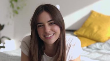 Evdeki yatakta yatarken kameraya gülümseyen güzel bir genç kadının portresi. Beyaz bir kadın yatak odasında dinleniyor. Pozitif duygu ve insanların kavramı.