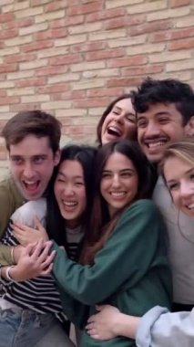 Mutlu bir grup genç öğrenci dışarıda gülüp birbirlerine sarılıyorlar. Milenyum 'dan arkadaş canlısı bir grup, şehir caddesinde birlikte eğleniyorlar. Dikey video.