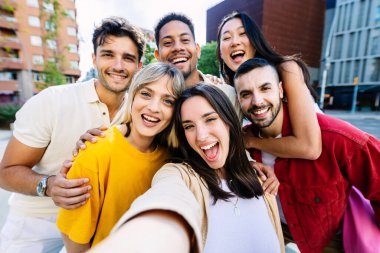 Çeşitli gençler dışarıda selfie çektirirken eğleniyorlar. Güzel kadın, üniversite öğrencisi arkadaşlarıyla birlikte kameraya gülümsüyor. Gençlik toplumu ve arkadaşlık kavramı.
