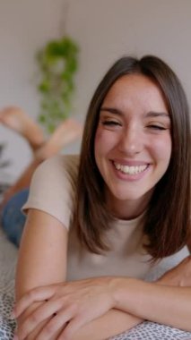 Evdeki yatakta kameraya gülümseyen güzel bir genç kadının dikey portresi. Neşeli, güzel, dişlek gülüşlü, kameraya bakan bin yıllık bir kadın..