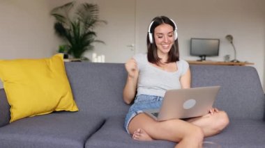 Dizüstü bilgisayardan konuşan mutlu genç bir kadın evden internetten ders çalışıyor. İnternetteki sanal eğitim sınıfına bağlanmış güzel bir öğrenci kız kanepede dinleniyor. Eğitim ve teknoloji kavramı.