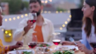 Bir grup genç, akşam çatı partisinde kırmızı şarap kadehleriyle tezahürat yapıyor. Çok ırklı arkadaşlar evde terasta bir araya gelip BQ yemeğini kutluyorlar.. 