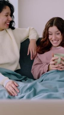 Mavi battaniyeyle kaplanmış, dizüstü bilgisayarda film seyreden iki genç kadının dikey videosu. Arkadaşlık ve multimedya yayın eğlence konsepti