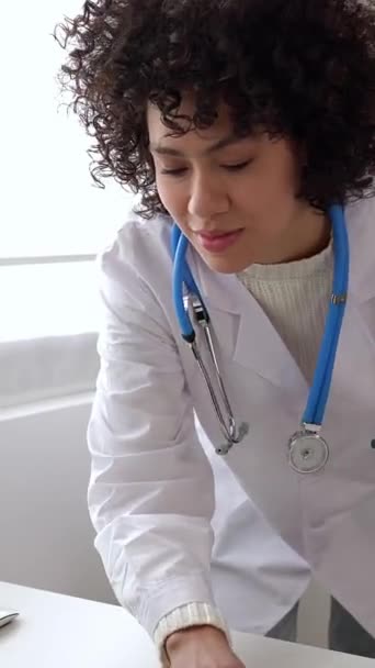 垂直录像 年轻的Latina医生在咨询过程中使用手机在笔记本电脑上工作 屏幕高清画面 — 图库视频影像
