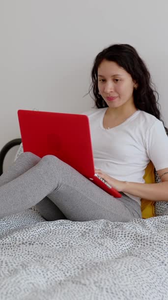 若いラテンアメリカの女性は 午前中にベッドでリラックスしたラップトップコンピュータを使用しています 教育と技術ライフスタイルの概念 縦型スクリーンビデオ映像 — ストック動画