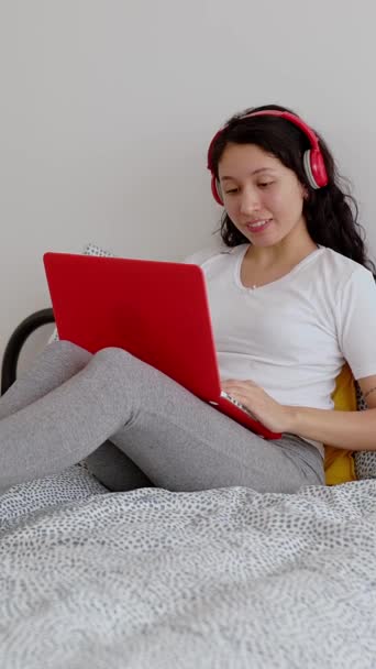 垂直ビデオ 午前中はノートパソコンを使ってヘッドフォンでラテンアメリカの若い女性を笑っています コンピュータでビデオ通話をしている100万人の少女 教育理念 — ストック動画