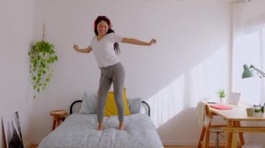 Yatakta dans eden kulaklıklarla müzik dinleyen neşeli genç Latin Amerikalı kız. Milenyum kadını yatak odasında eğleniyor. Gençlik yaşam tarzı konsepti