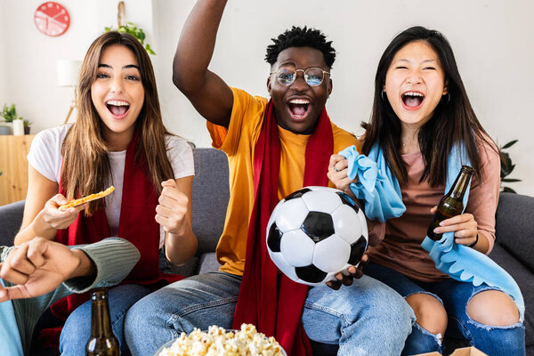 Diverse young friends watching a football match on TV at home. Sports entertainment concept.