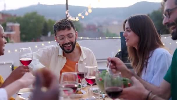 屋上テラスでテーブルの周りに座っている外でBbq夏のディナーパーティーを楽しむ多種多様な若い幸せな友人 ミレニアル世代の人々は 日没の間に食事を楽しんで 一緒に祝い 楽しんでいる — ストック動画