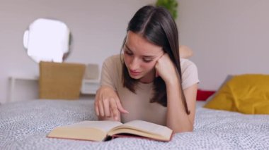 Genç ve güzel bir kadın yatakta kitap okuyor. Boş zaman aktiviteleri ve ev hayatı konsepti.