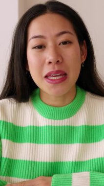 Dikey video. POV - Asyalı genç bir kadının evdeki oturma odasındaki kameraya çevrimiçi bir video konuşması. Sohbet video konferansı sırasında neşeli Çinli kız