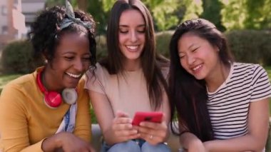 Açık havada birlikte akıllı cep telefonu kullanan mutlu, çok ırklı genç bayan arkadaşlar. Üç bin yıllık çeşitlilikte kadın dışarıda geçirdiği yaz tatilinin tadını çıkarırken elinde akıllı telefon tutuyordu..