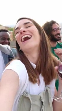 Genç bir grup insan çatıdaki partide eğleniyor. Terasta barbekü yemeği sırasında akıllı telefon kamerasıyla video selfie çeken çok ırklı arkadaşların bakış açısı. Dikey ekran video.