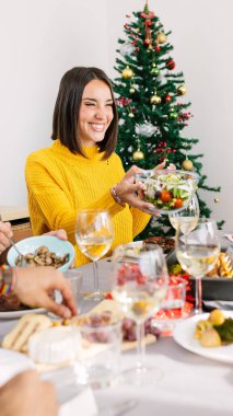 Noel kutlaması sırasında yemek masasında salata servisi yapan mutlu genç bir kadının dikey çekimi. Aile ve xmas tatil konsepti.