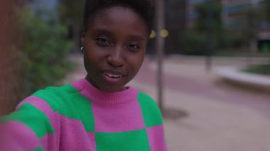 Mutlu, genç Afrikalı bir kadın şehir dışında otururken arkadaşıyla cep telefonu uygulaması kullanarak görüntülü konuşma yapıyor. Ekran aygıtı görüntüsü. El sallıyor..