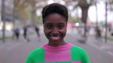 Şehrin arka planında kameraya gülümseyen Afrikalı genç bir kadının portresi. Açık havada duran siyah bir kadının vesikalığı..