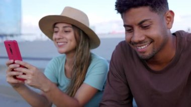 Açık havada cep telefonu kullanan iki genç Latin arkadaş. Çok ırklı turist bir çift akıllı telefon uygulamasında sosyal medya içeriğini izlemek için şehir caddesinde mola veriyor. Teknoloji konsepti.