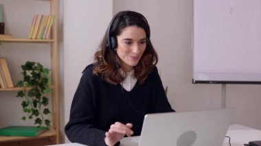 Kulaklık takmış genç bir iş kadını laptopta iş arkadaşıyla konuşuyor. Kendine güvenen profesyonel bir kadın partneriyle çevrimiçi sohbet ediyor. İş ve insan kavramı.