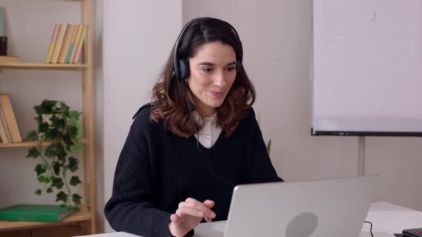 年轻的女商人戴着耳机和同事在办公室里用手提电脑视频通话 自信的职业女性与伴侣进行在线对话 商业和人的概念 — 图库视频影像