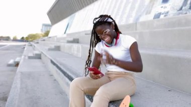 Vitiligo 'su olan Afrikalı genç bir kız dışarıda cep telefonuyla eğleniyor. Gençlik kültürü ve teknoloji kavramı. Metin için alanı kopyala.