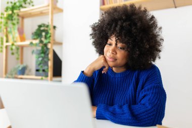 Genç Afro-Amerikan kadın dizüstü bilgisayarla çalışıyor. Konsantre iş kadını bilgisayar ekranına bakıyor bir iş makalesi okuyor ya da sanal video eğitimi dersinde dinliyor. İş konsepti