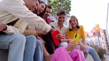 Genç bir grup insan dışarıda cep telefonuyla eğleniyor. Akıllı telefon uygulamasında sosyal medyadan keyif alan neşeli öğrenci topluluğu.