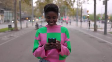 Genç mutlu zenci kadın şehir caddesinde cep telefonu kullanıyor. Metin için şehir arkaplanı ve kopyalama alanı.