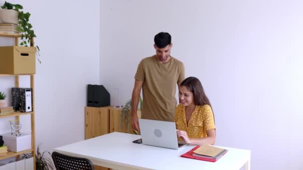 オフィスで一緒にラップトップコンピュータで働く2人の幸せな人 職場で男性同僚と話し合っている若い成人女性 ビジネスコンセプト — ストック動画