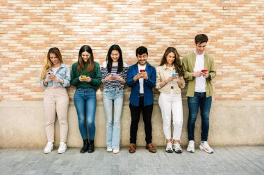 Duvar arkasına yaslanmış cep telefonu kullanan mutlu bir grup genç. Milenyum arkadaş nesli gülüyor ve eğleniyor. Akıllı telefondan sosyal medya ağına bağlanıyor..